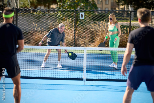 A mixed age and sex group of pickleball players hit balls on a blue court