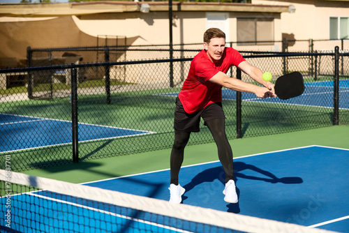 A mustached man wearing a red shirt plays pickleball