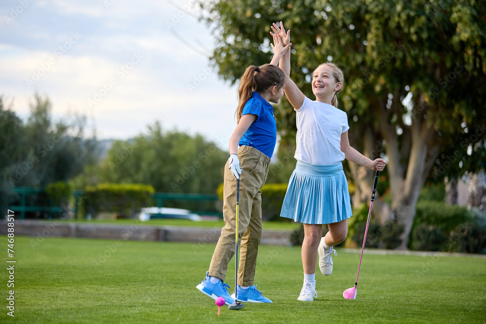 Two young girls play golf on a tee box Two young girls play golf on a tee box