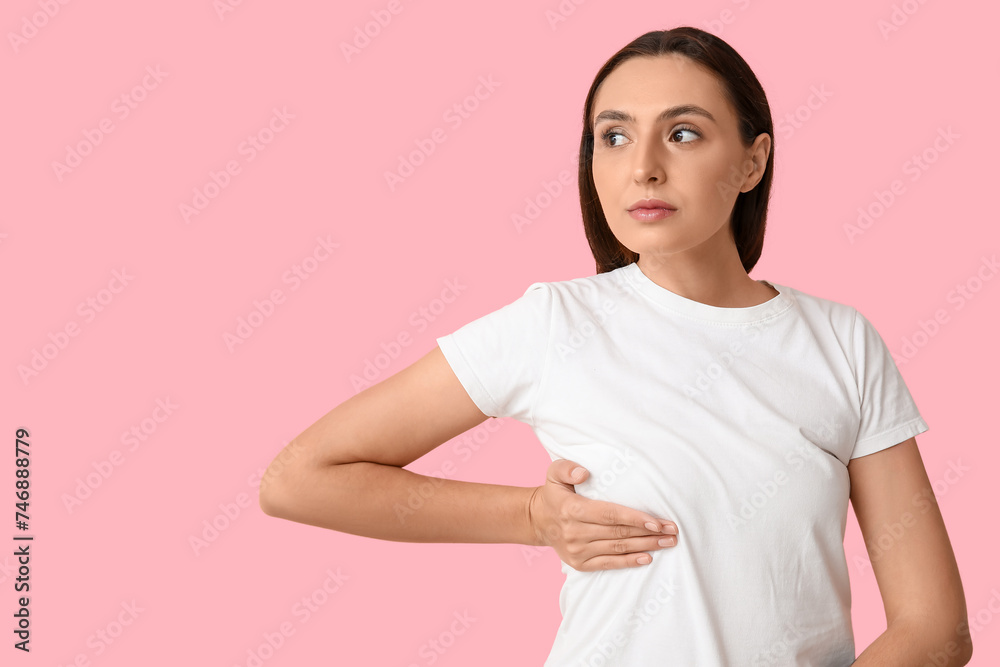 Obraz premium Young woman checking her breast on pink background. Cancer awareness concept