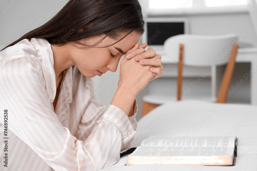 Beautiful young woman reading Bible and praying in bedroom Beautiful young woman reading Bible and praying in bedroom