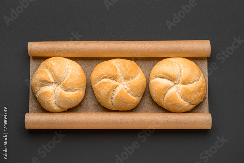 Baking paper with delicious kaiser rolls on black background photo