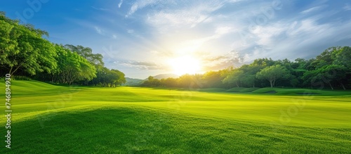 The sun shines brightly over a lush green golf course, highlighting the vibrant green grass and manicured landscape. The peaceful atmosphere is perfect for a day of golfing under the clear blue sky.