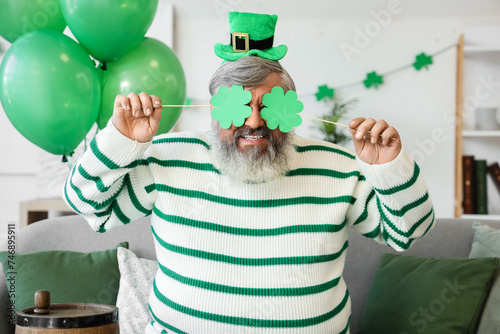 Mature man in hat with paper clovers at home on St. Patrick's Day