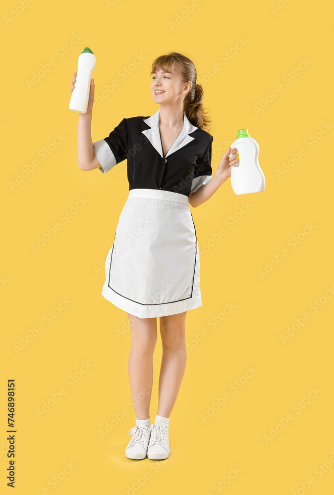 Young chambermaid with bottles of detergent on yellow background Young chambermaid with bottles of detergent on yellow background