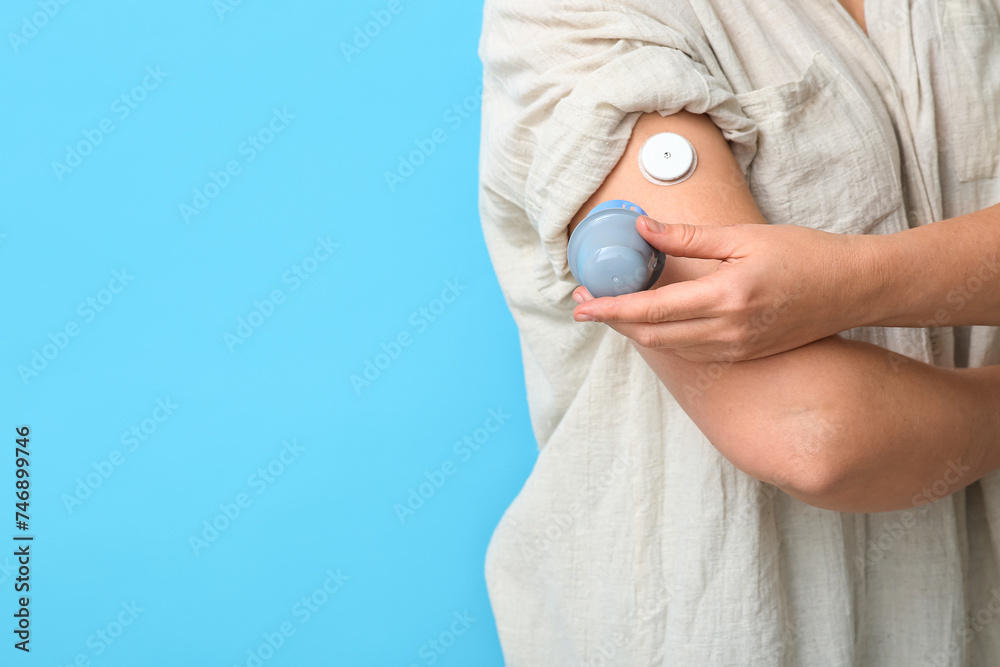 Fototapeta premium Woman with glucose sensor for measuring blood sugar level and applicator on blue background, closeup. Diabetes concept