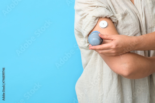 Woman with glucose sensor for measuring blood sugar level and applicator on blue background, closeup. Diabetes concept photo