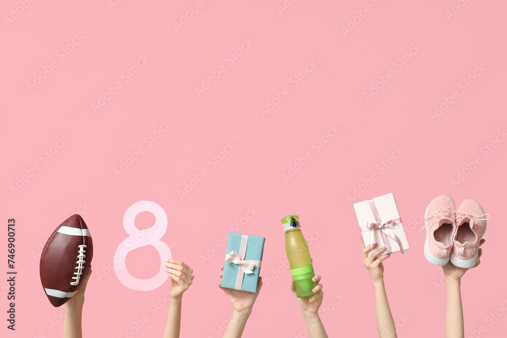 Female hands with sports equipment, paper figure 8 and gifts for International Women's Day on pink background