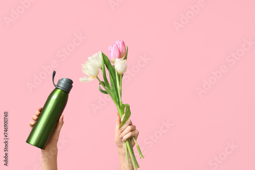 Female hands with sports bottle of water and bouquet of tulip flowers for International Women's Day on pink background