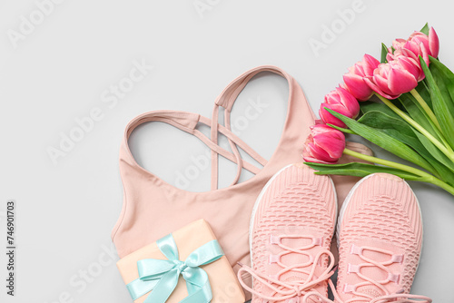Sports bra, shoes, gift box and tulip flowers for International Women's Day on light background photo