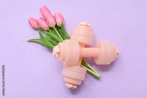 Pair of dumbbells and beautiful tulip flowers for International Women's Day on lilac background #746902156