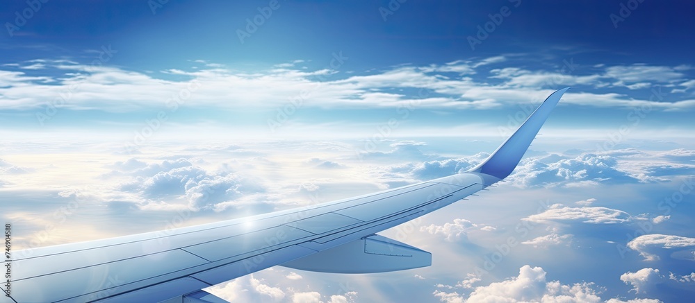 The image shows a perspective from inside an airplane cabin, with clouds outside the window and the wing of the aircraft visible. The airplane is soaring through the sky, offering a unique view of the The image shows a perspective from inside an airplane cabin, with clouds outside the window and the wing of the aircraft visible. The airplane is soaring through the sky, offering a unique view of the