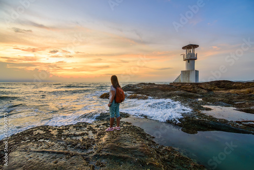 Woman backpacker solo travel alone standing on a rock with sunset sky at sea in Khao Lak Phuket Thailand. photo