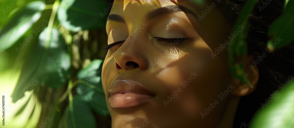 A close-up view of a woman with her eyes shut, showcasing a serene expression, against a backdrop of trees highlighting natures beauty and organic connection. A close-up view of a woman with her eyes shut, showcasing a serene expression, against a backdrop of trees highlighting natures beauty and organic connection.