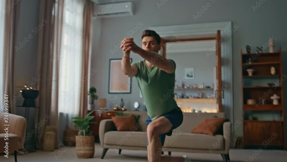 Active sportsman making squats in living room. Focused young man training body Active sportsman making squats in living room. Focused young man training body