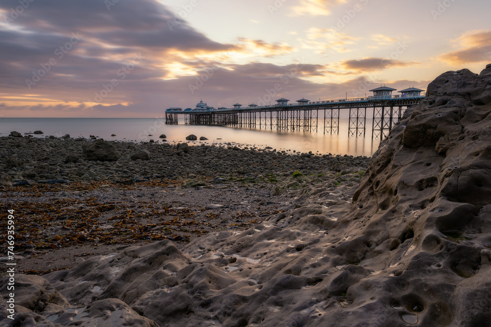 Sunrise over the rugged rocky coastline with Llandudno Pier in the background - North Wales, United Kingdom