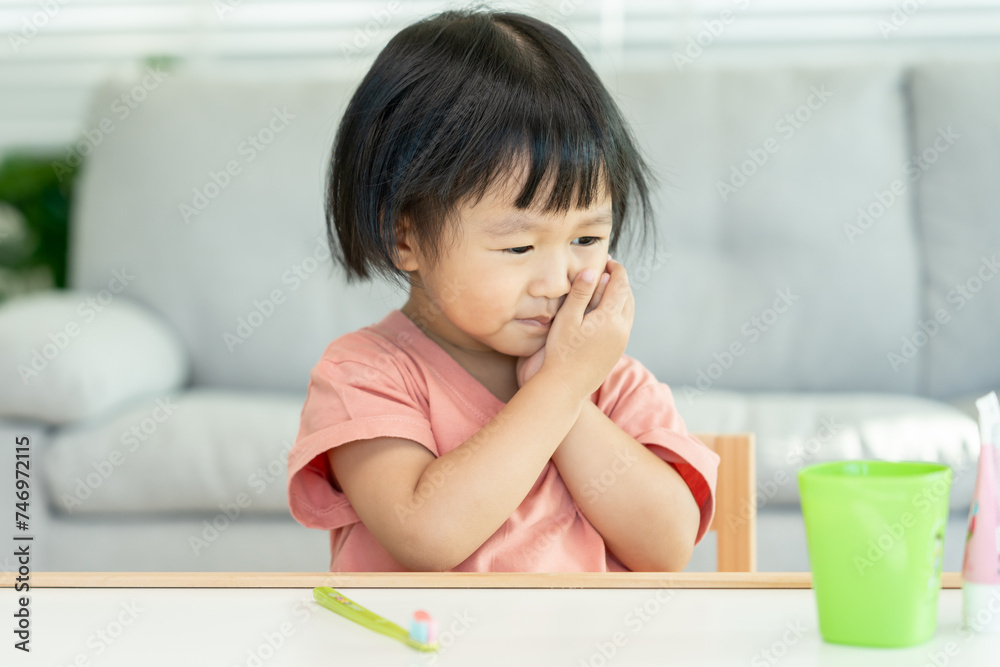 little asian girl presses hand to cheek, suffers from pain in tooth. Teeth decay, dental problems, child emotions and facial expression, oral health care, reducing sweets, fluorine coating little asian girl presses hand to cheek, suffers from pain in tooth. Teeth decay, dental problems, child emotions and facial expression, oral health care, reducing sweets, fluorine coating