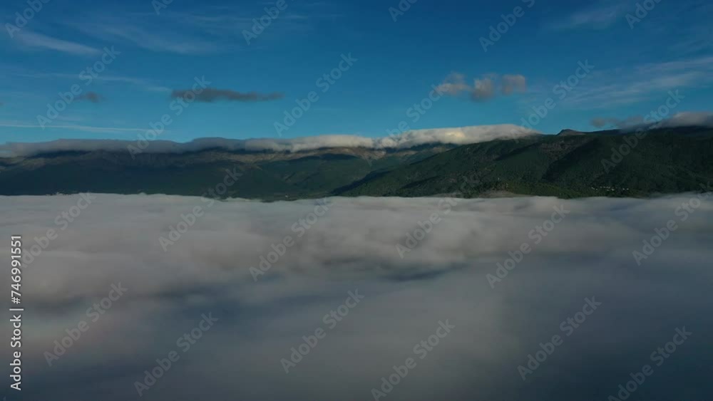 lateral flight with a drone over a sea of clouds visualizing a large mountain system with forests that in turn has a chain of clouds in its peaks at dawn in a valley with a blue sky in Avila Spain lateral flight with a drone over a sea of clouds visualizing a large mountain system with forests that in turn has a chain of clouds in its peaks at dawn in a valley with a blue sky in Avila Spain