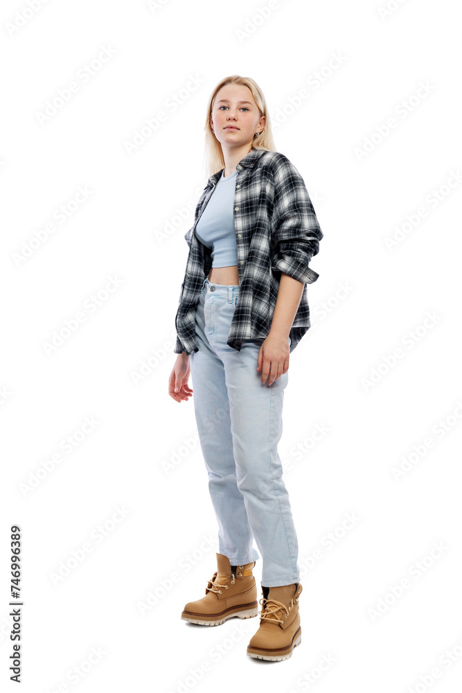 Fototapeta premium A teenage girl is standing. A cute blonde with freckles on her face wearing jeans, a plaid shirt and yellow shoes. Full height. Isolated on a white background. Vertical.