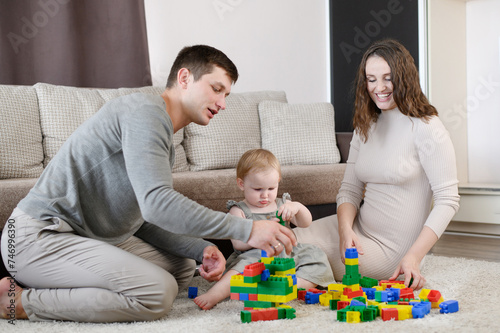 Young family: dad, mom playing with a child with a multicolor plastic construction set,sitting on floor at home,having fun together on weekend, family vacation. Educational game for children, leisure