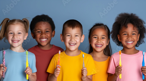 Diverse group of kids in bright shirts holding up toothbrushes and smiling. Concept for good oral health at young age.