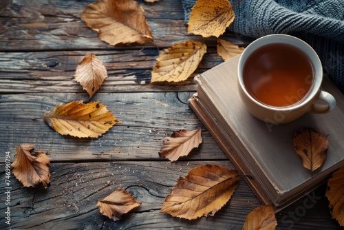 Cozy autumn flat lay with a knitted sweater, an open book, a cup of tea, and scattered maple leaves on a wooden background. © evgenia_lo