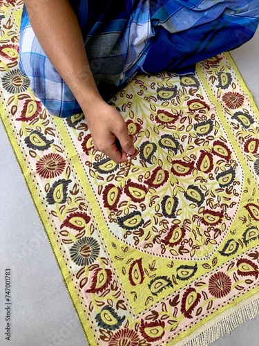 Yellow sajadah and blue sarong. With hand holding tasbih. Sholat photo