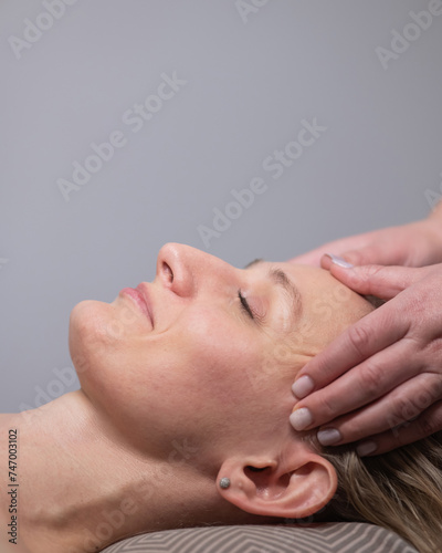 Caucasian woman undergoing a head and face massage procedure. Vertical photo.