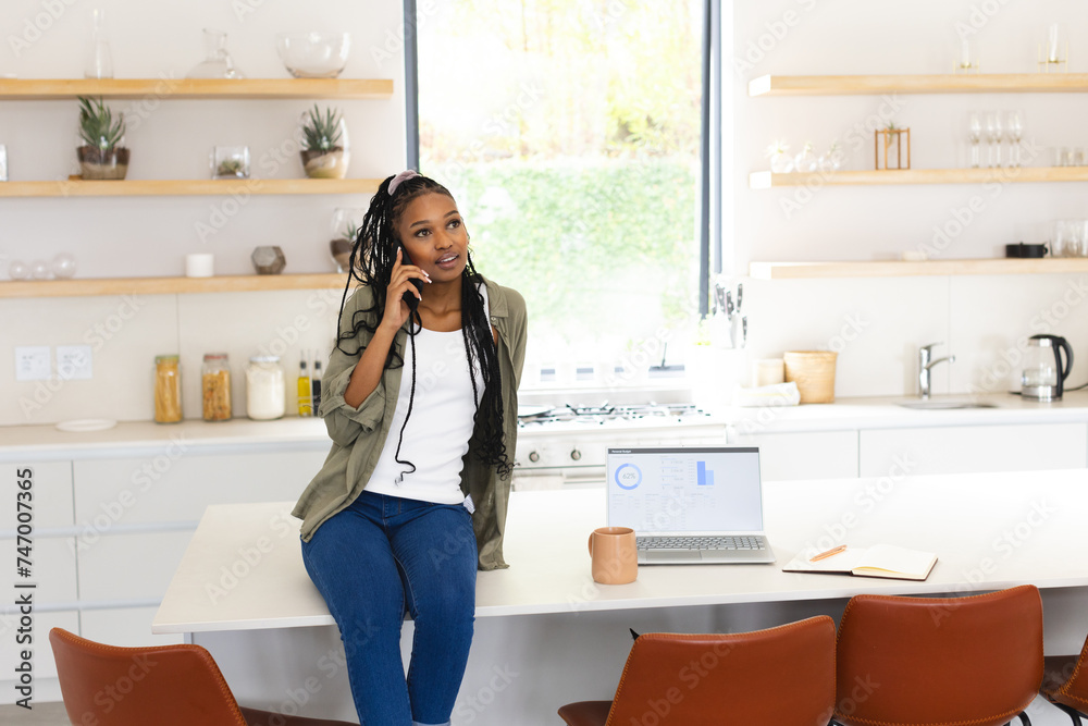 A young African American woman chats on the phone, leaning on a kitchen island with copy space A young African American woman chats on the phone, leaning on a kitchen island with copy space