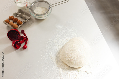 A mound of flour with dough sits on a kitchen counter with copy space, surrounded by baking ingredie