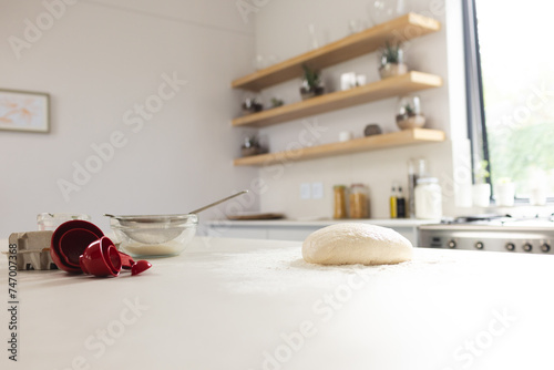 A kitchen counter is dusted with flour, featuring dough and a red measuring cup with copy space