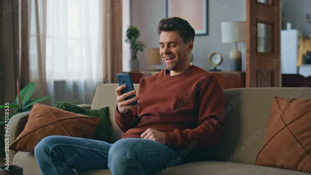 Laughing guy looking smartphone funny videos at couch. Man browsing news feed Laughing guy looking smartphone funny videos at couch. Man browsing news feed