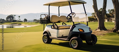 A golf cart is parked on the lush green fairway of a golf course, ready for a round of golf. The cart is stationary, surrounded by a well-maintained course, under a clear blue sky.