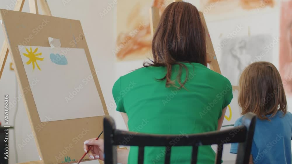 Vidéo Stock Adult supervising a child painting on canvas in an art ...