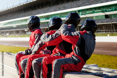A team of racing drivers in matching red suits taking a break at the racetrack.  photo