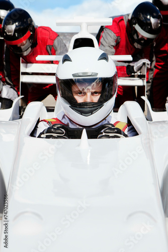 Focused racecar driver ready on the track with pit crew in the background. 