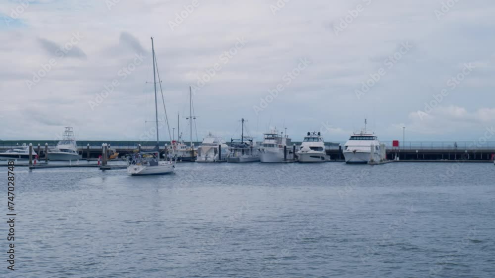 A small white sailing boat has entered the marina and is preparing to dock, with other larger boats moored nearby. Handheld camera, in 4K A small white sailing boat has entered the marina and is preparing to dock, with other larger boats moored nearby. Handheld camera, in 4K
