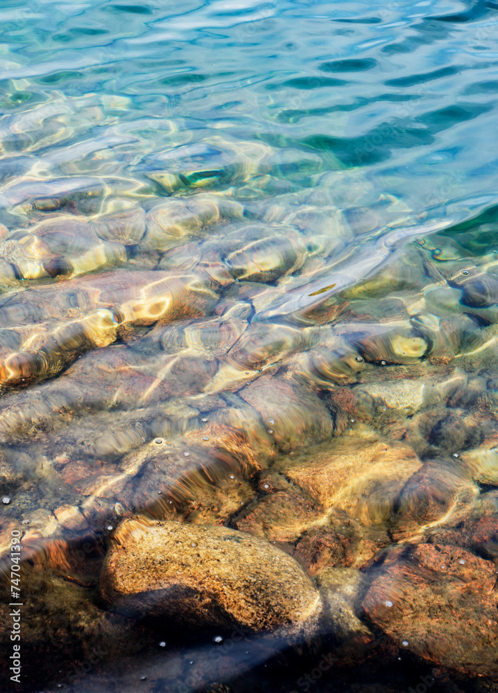 The rocks on the lake bottom are seen through clear water with small waves distorting the view, Finnish Lapland