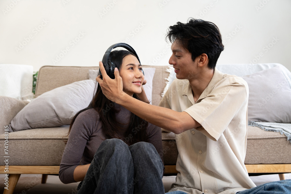 Happy couple asian young women happy playing with headphones while spending time together couch in living room at home