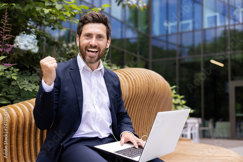 Successful businessman with laptop celebrating achievement outdoors