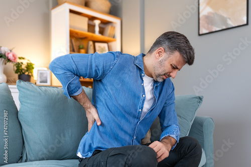 Handsome man touching his back, suffering from backpain, sciatica, sedentary lifestyle concept. Spine health problems. Healthcare, insurance photo
