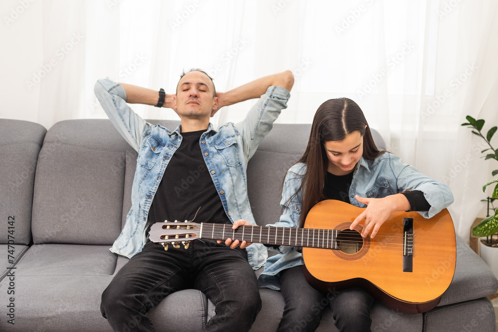 Obraz premium Father guy teaching girl teenager daughter guitar playing at home. Family musical lessons with strings instrument