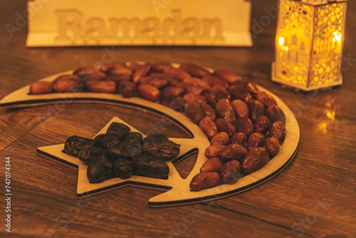 Ramadan Kareem. Dates on wooden tray in the shape of a month and a star and oriental wooden Lantern lamps on wood background. Islamic Holy Month Greeting Card. Soft focus. Shallow DOF.