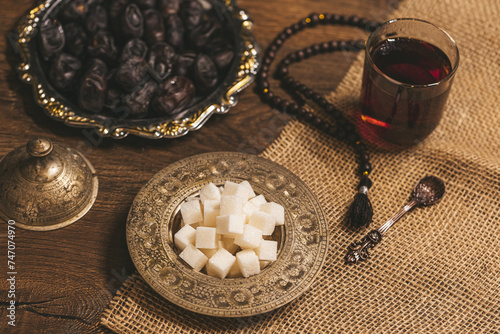Glass of tea with sugar and dried dates on a wooden background with burlap. Ramadan Kareem holiday background. Halal meal set for fasting is obligatory for Muslim on wooden. . Soft focus. Shallow DOF.