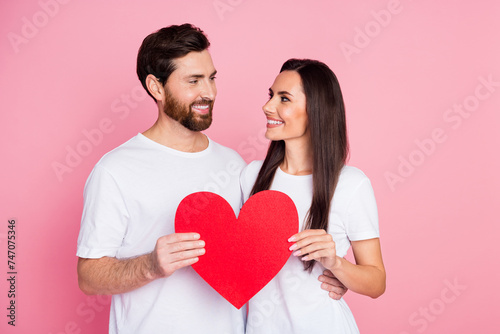 Photo portrait of lovely young couple hold red heart postcard look each other wear trendy white outfit isolated on pink color background