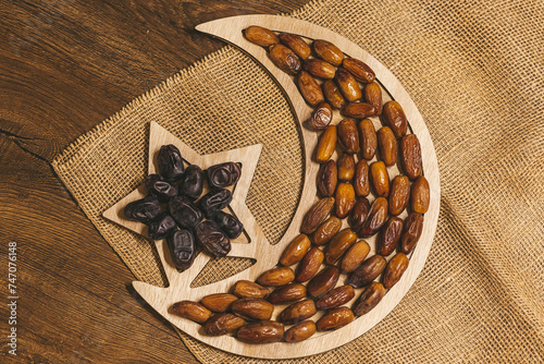 Dried dates on a tray in the shape of a month and a star on a wooden background with burlap. Ramadan Kareem holiday background. Islamic Holy Month Greeting Card. Soft focus. Shallow DOF.