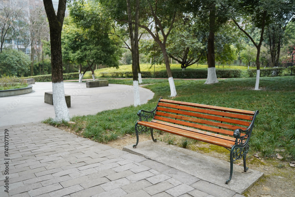 A park bench, standing silently in an environment surrounded by lush trees. The area around the bench is covered in grass and additional trees, A park bench, standing silently in an environment surrounded by lush trees. The area around the bench is covered in grass and additional trees,