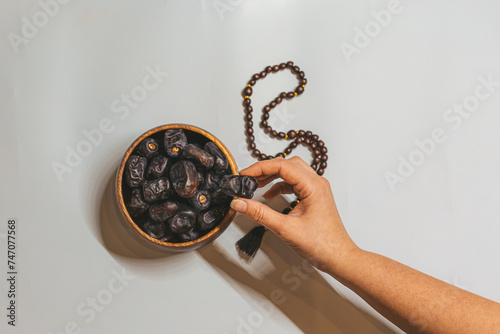 A wooden bowl with dried dates, a wooden rosary and a date in a woman's hand. Ramadan Kareem holiday concept