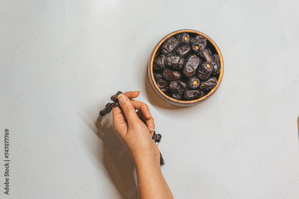 Φωτογραφία Wooden rosary in a woman's hand and dried dates in a wooden bowl