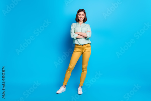 Full size photo of gorgeous pleasant nice woman dressed teal shirt yellow trousers keep arms folded isolated on blue color background